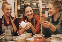 A Company Of Three Pretty Young Women Friends Make Ceramic Mugs In A Pottery Workshop.