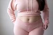 Close-up view of a woman belly in sports clothes on grey background, obesity concept