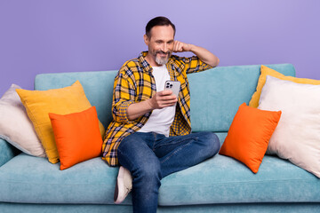 Poster - Photo of bearded cheerful man freelancer wear stylish clothes sit divan free time relax after work day isolated on purple color background