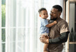 Portrait happy African American father with baby in arms standing near window at home	