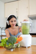© bongkarn - A gorgeous Asian woman in sportswear is making her healthy green detox smoothie in the kitchen.