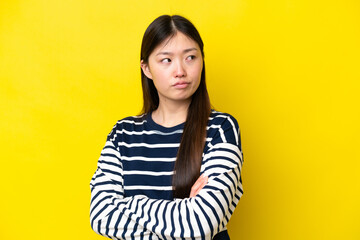 Wall Mural - Young Chinese woman isolated on yellow background keeping the arms crossed