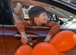 © Alexandra - kid boy with orange balloons and spider web on face in car, with head from window or outside from panoramic sunroof.child cover face with ballon, raised hands.serious face boy, halloween