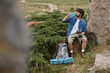 © LIGHTFIELD STUDIOS - tourist and nature concept, indian man drinking water and holding camera while sitting on rock