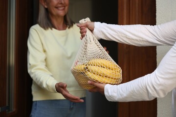 Poster - Helping neighbours. Man with net bag of products visiting senior woman outdoors, closeup