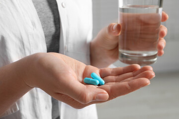  Woman with glass of water and pills on blurred background, closeup