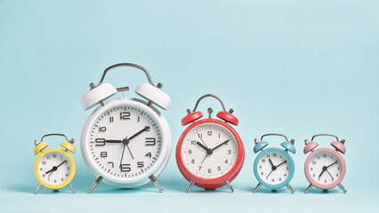 Five alarm clocks of different colors show different times. Start of the day, waking up, morning, different time zones.