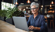 Elderly Lady, old granny, Wearing Glasses, Works on Laptop in a Cafe Setting, Senior Adult Engaged with Computer