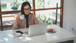 © panadesignteam - Asian businesswoman working on a laptop while drinking a cup of coffee in a cafe
