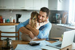 © Geber86 - Young single father finding hope in his daughters embrace while stressing over bills and home finances in the morning in the kitchen