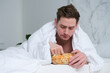 © Евгений Шемякин - Young man eating chips in bed, bedroom. Fast junk food.