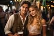 © Irina - A couple looks and smiles into the camera and says cheers or toasts with a mug of beer in the Bavarian beer garden or at Oktoberfest.