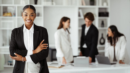 Wall Mural - Happy black businesswoman posing with folded arms and smiling, posing during meeting with colleagues in office