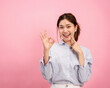 © Katcha - Young asian woman wearing long sleeve shirt and smiling while touching forefinger on the face and showing ok