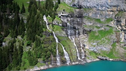 Poster - Idyllic swiss mountain lake Oeschinensee (Oeschinen) with waterfall and snowy peaks of Alps mountains near Kandersteg town. aerial drone panoramic video 4k. Switzerland nature scenery