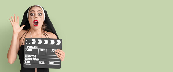 Shocked young woman dressed for Halloween as nun with clapperboard on green background with space for text