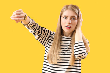 Wall Mural - Stressed young woman looking at wristwatch on yellow background. Deadline concept