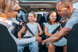 © Soloviova Liudmyla - Inside car photo of mother and father fastening with safety auto belts their little daughters girl sitting in child seat and listening headphones. Family values, traveling and technology concept.