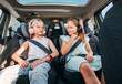 © Soloviova Liudmyla - Portrait of two positive smiling sisters sitting in child car seats fastening safety belts listening to music using headphones. Happy childhood, auto journey concept image.