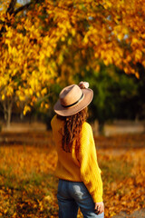 Autumn mood. Happy woman in a bright sweater and hat having fun, walking, having a picnic in an autumn park at sunset. The concept of relaxation, walking.