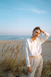© maxbelchenko - Stylish woman posing on autumn beach in wild grass. A woman enjoys the autumn nature on the beach, relaxing. Fashion, style and relaxation concept.