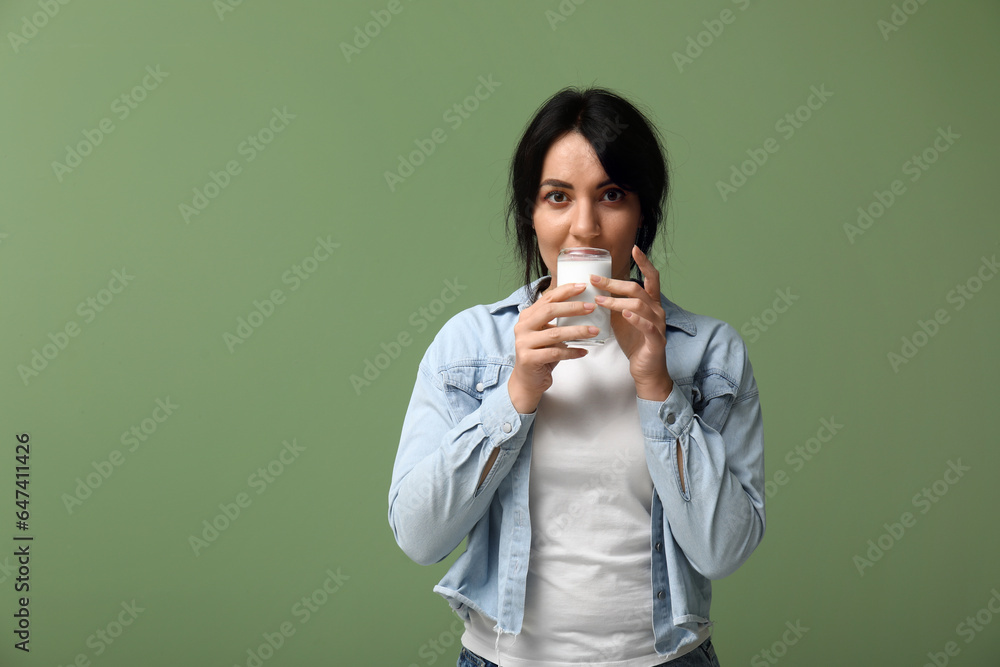 Pretty young woman drinking milk on green background