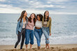 © PintoArt - A diverse group of female friends on the beach, laughing and enjoying themselves on a cloudy day, find beauty in each other's company regardless of the weather
