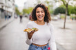 © PintoArt - Hispanic curvy woman eating a pizza on the street