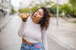 © PintoArt - A Hispanic curvy woman indulges in a slice of pizza on the bustling street, savoring the flavors of both her culture and her cravings