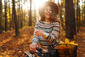 A beautiful woman in stylish clothes and a hat walks and rides a bike in a sunny autumn park. Concept of nature, relaxation. Lifestyle.