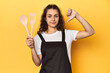Woman with apron, wooden cooking utensils, yellow, showing a dislike gesture, thumbs down. Disagreement concept.
