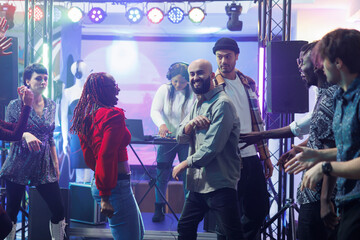 Cheerful diverse couple laughing while improvising dance battle at nightclub discotheque. Happy carefree people showing moves on crowded dancefloor and having fun while clubbing at night
