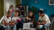 © kinomaster - Medium shot of a group of teens, young people, friends studying, preparing for an exam, discussing, looking at their notes, using devices, watching something.