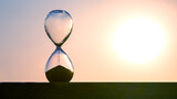Fototapeta  - Hourglass counts the length of time against the background of the evening sun. The concept of the fluidity of life time in the universe. time and light