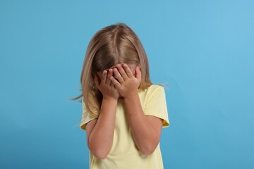 Wall Mural - Resentful girl covering face with hands on light blue background