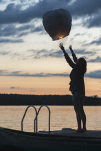 Silhouette Of A Girl Releasing A Lit Paper Lantern Into The Air At Sunset; Lake Of The Woods, Ontario, Canada