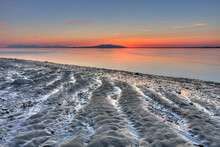 Ripples And Patterns In The Sand At The Waters Edge With A Pink Sunset On The Horizon