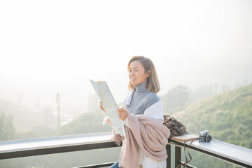 Wall Mural - Girl tourist in mountain read the map and looking mountain view at countryside homestay in the morning sunrise with copy space. journey, trip and relaxing concept. coats blankets in winter.