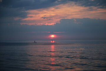 Poster - Sunset above the sea with small figures of people sailing on supboards, selective focus