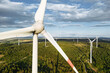 Wind turbines in a hilly forest in front of a partly cloudy, but sunny sky are seen from an aerial view during sunset