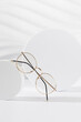 © Dina Photo Stories - Unisex eyeglasses in a golden metallic frame on podium on white background. Vertical, close up. The product minimal still life. Optic store discount, sale. Copy space. Trendy eyewear photography
