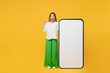 © ViDi Studio - Full body young cool caucasian happy woman she wears white shirt casual clothes big huge blank screen mobile cell phone smartphone with area point index finger up isolated on plain yellow background.