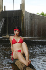 Wall Mural - A pretty Asian female in a swimsuit sits, relaxes and shows off her expressions of fun. At a spillway in Thailand.