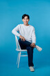 © makistock - Photo of young guy smiling sitting chair empty space isolated blue color background