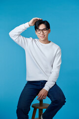 Wall Mural - Vertical shot of a young cheerful man sitting on a chair isolated on blue background