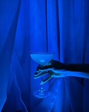 Close-up Of A Woman's Hand Holding A Cocktail Against A Blue Curtain
