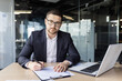 © Tetiana - Portrait of a young lawyer. a notary who is concentrating on working in the office with a laptop and documents, looks confidently into the camera