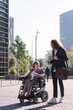 © Raul Mellado - business man and woman in wheelchair talking while walking between office buildings in financial district, concept of diversity and urban lifestyle, copy space for text