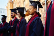 © AnnaStills - Happy students in robes standing in a row and listening to speaker