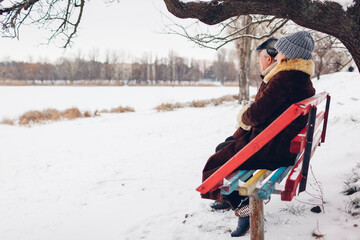 Wall Mural - Senior family couple sitting on bench outdoors during snowy winter weather. Elderly people enjoy landscape. Space